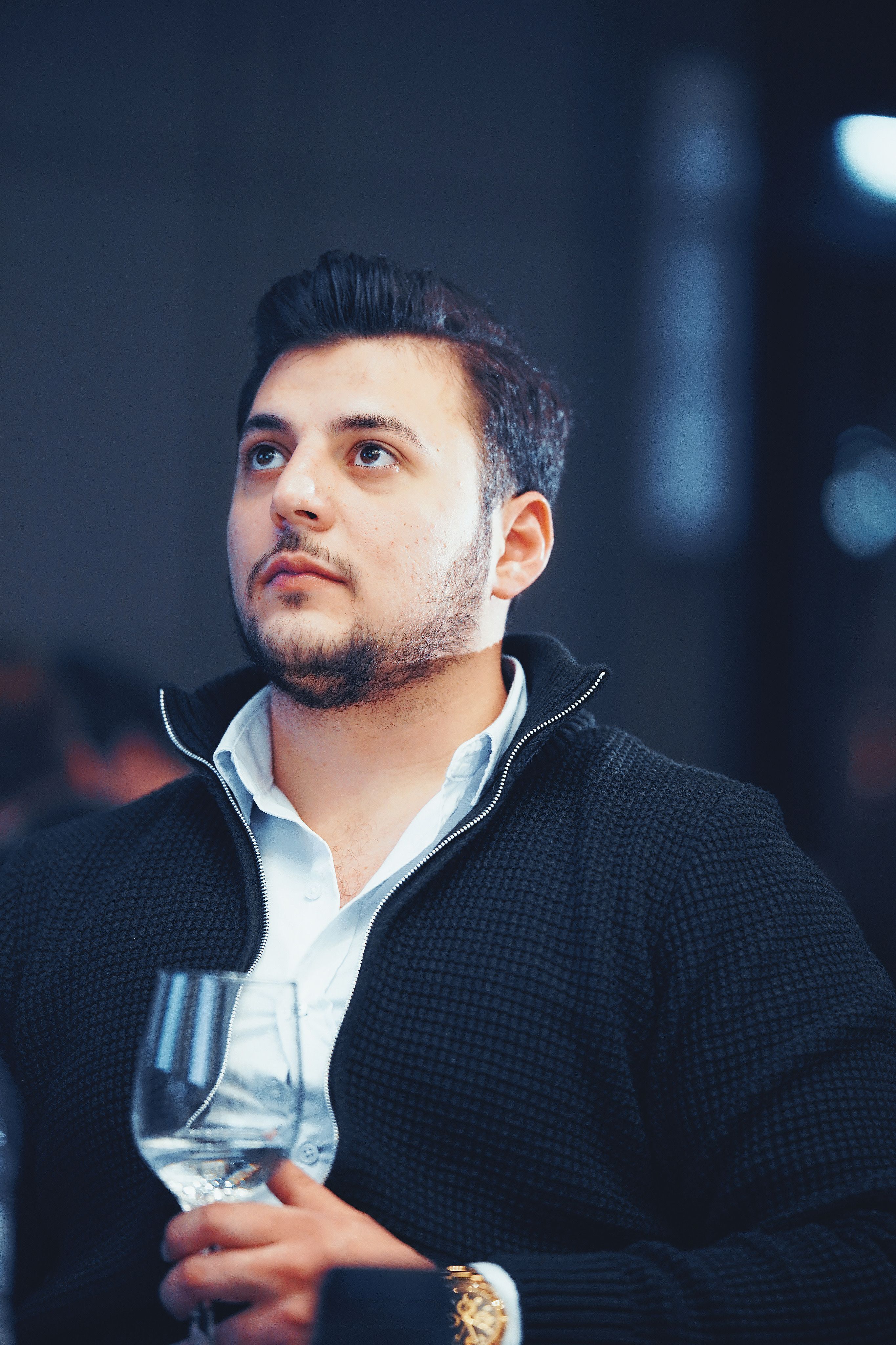 A stylish man in business casual attire holding a wine glass indoors in Istanbul.