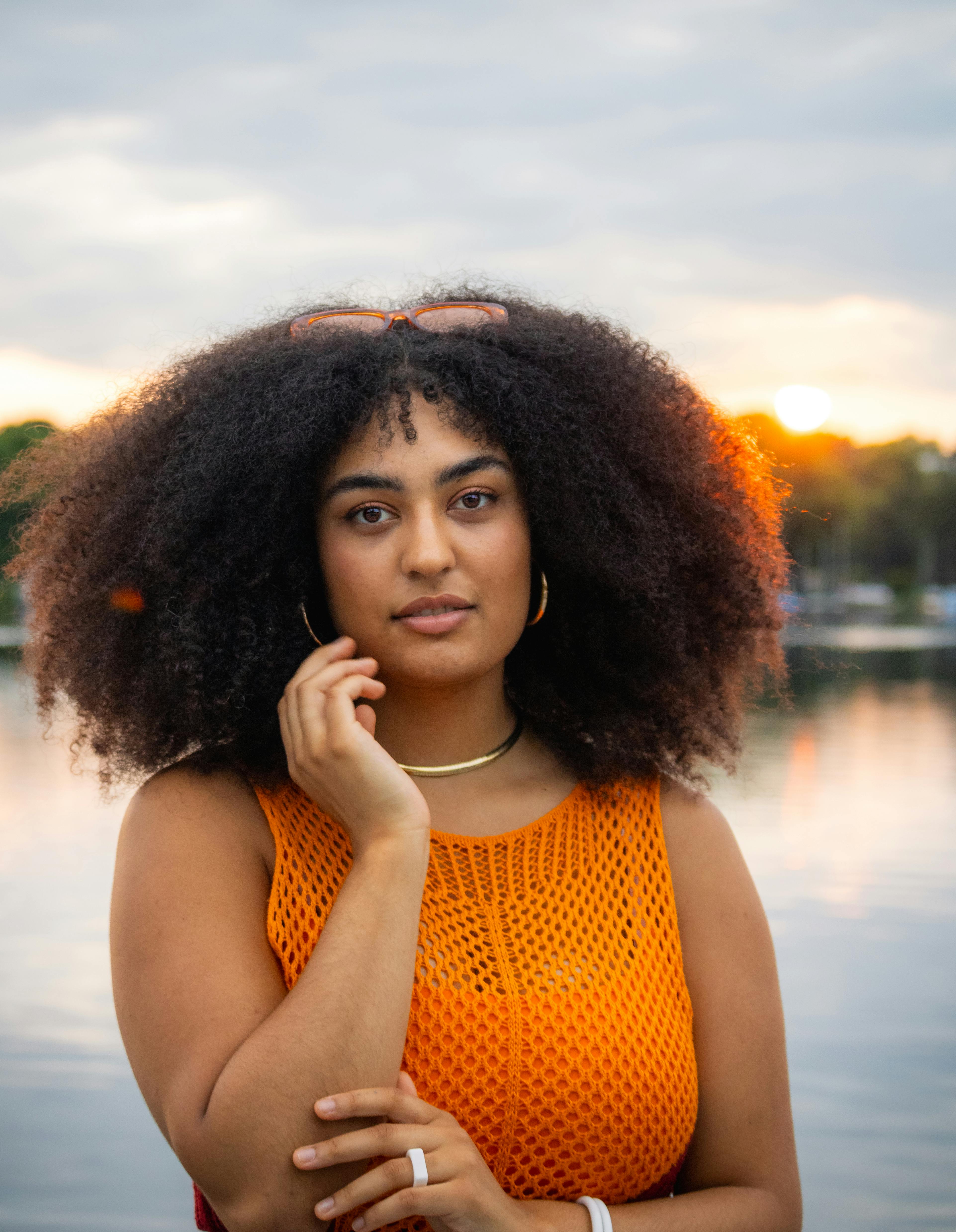 a woman with an afro wearing an orange top and a necklace