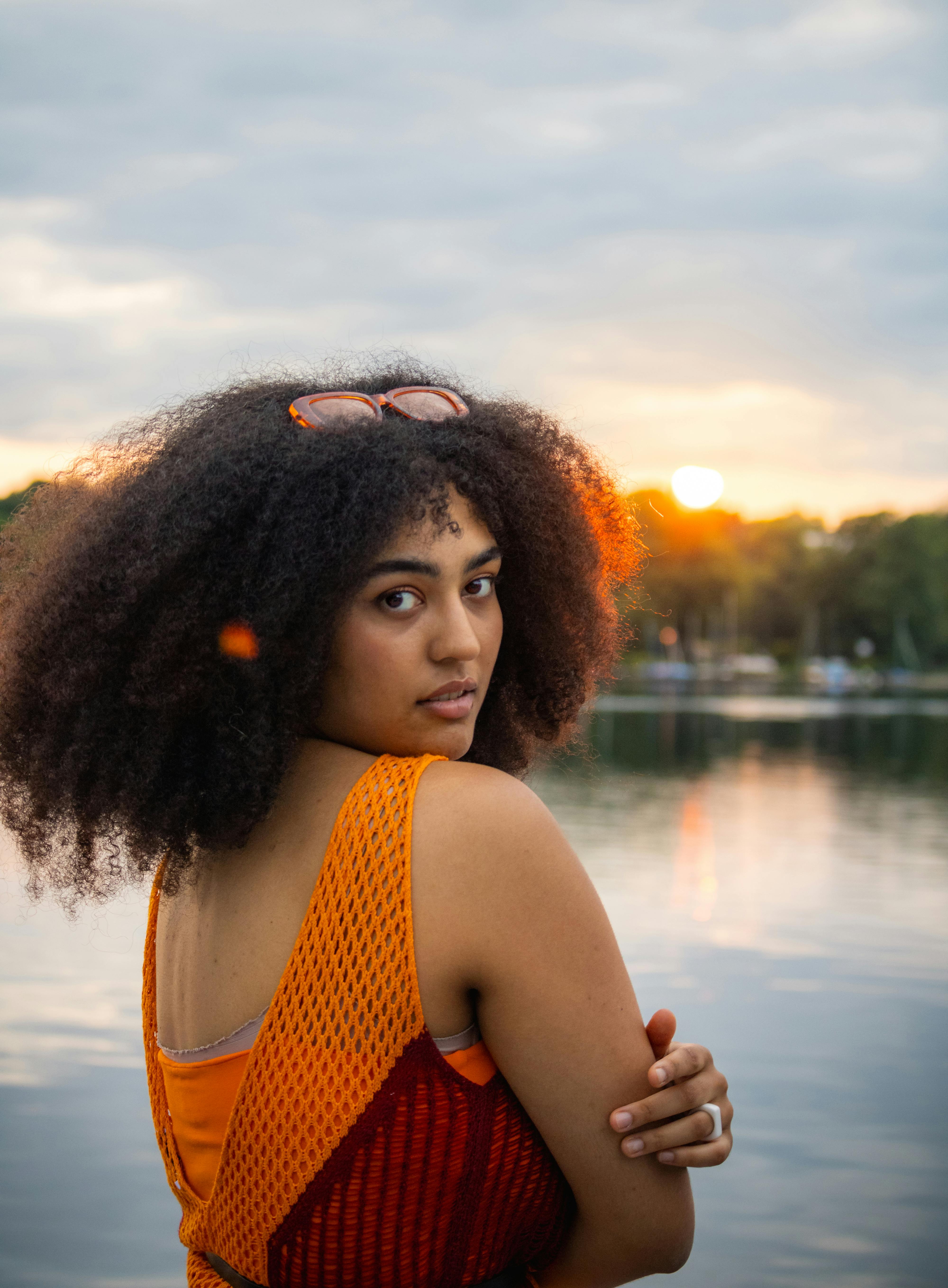 a woman with an afro standing in front of a lake