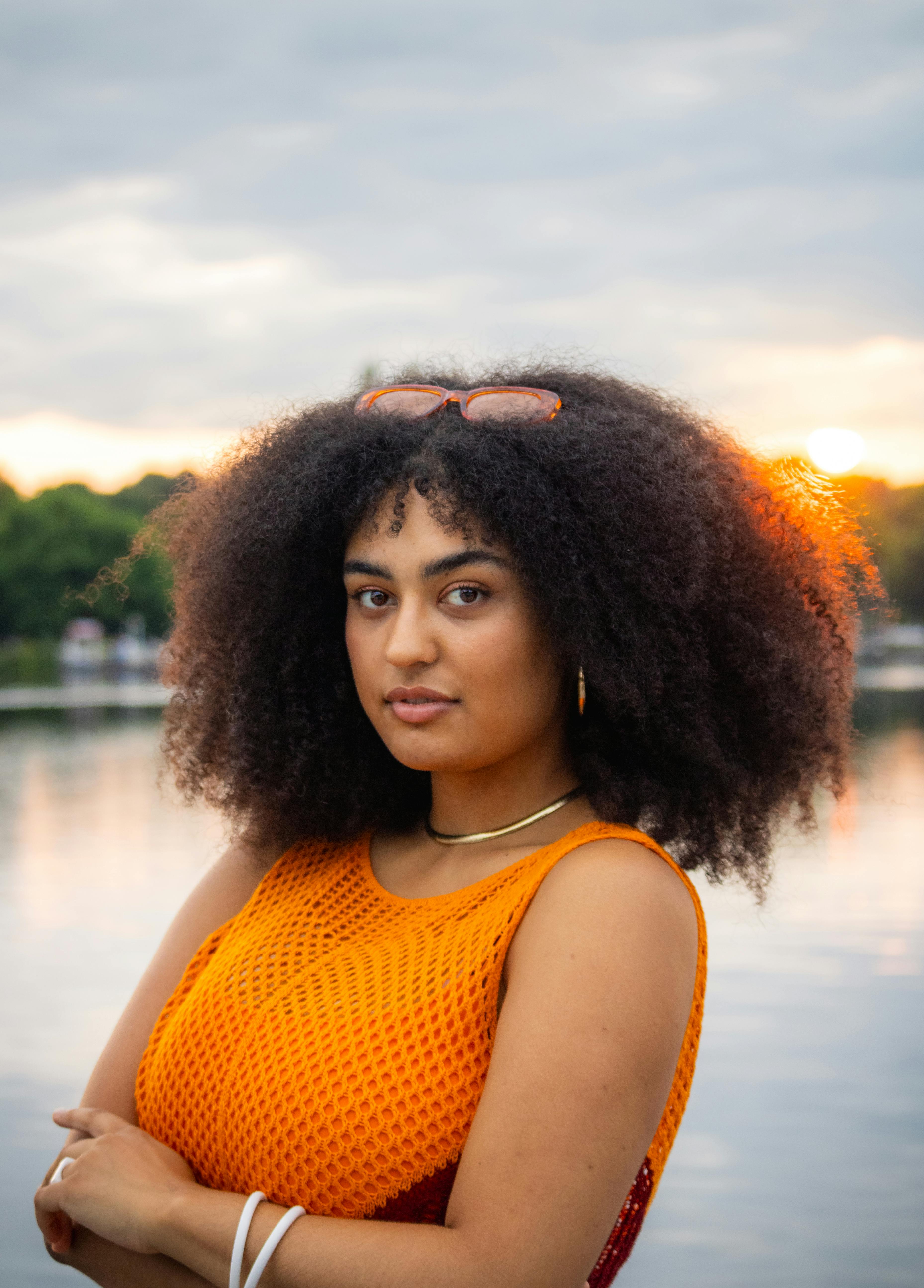 a woman with an afro wearing an orange top and a necklace