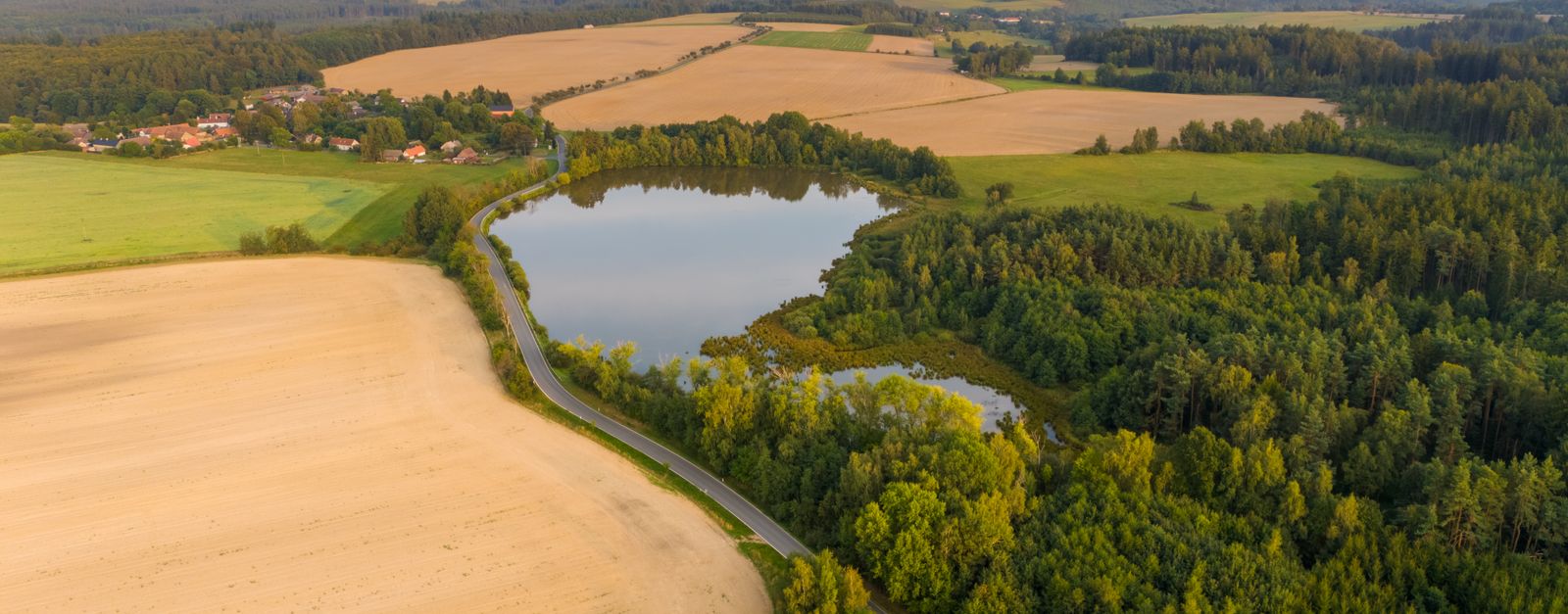 Aerial view of Chlístovice countryside with fields, forest, and lake.