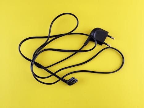 Close-up of a tangled black power cord placed on a vibrant yellow background.