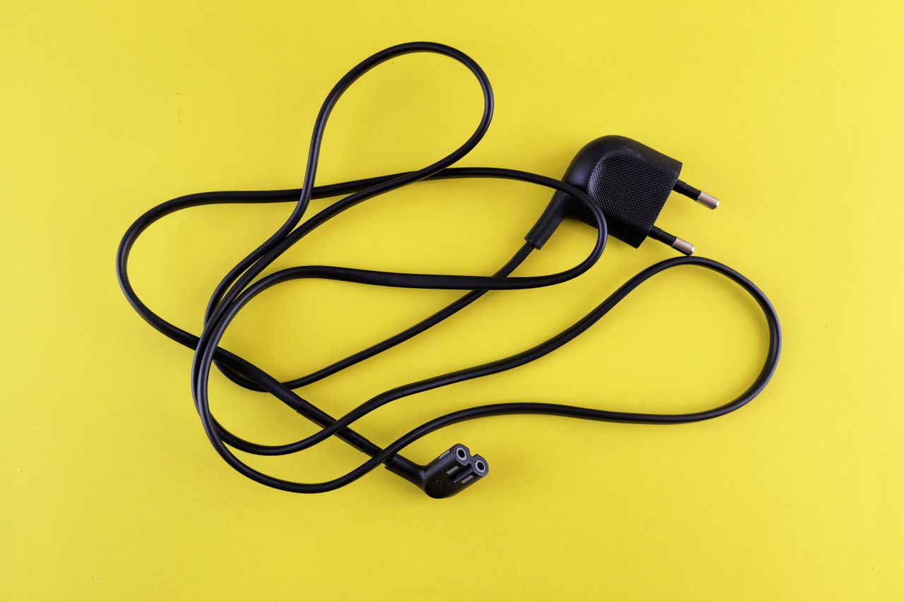 Close-up of a tangled black power cord placed on a vibrant yellow background.