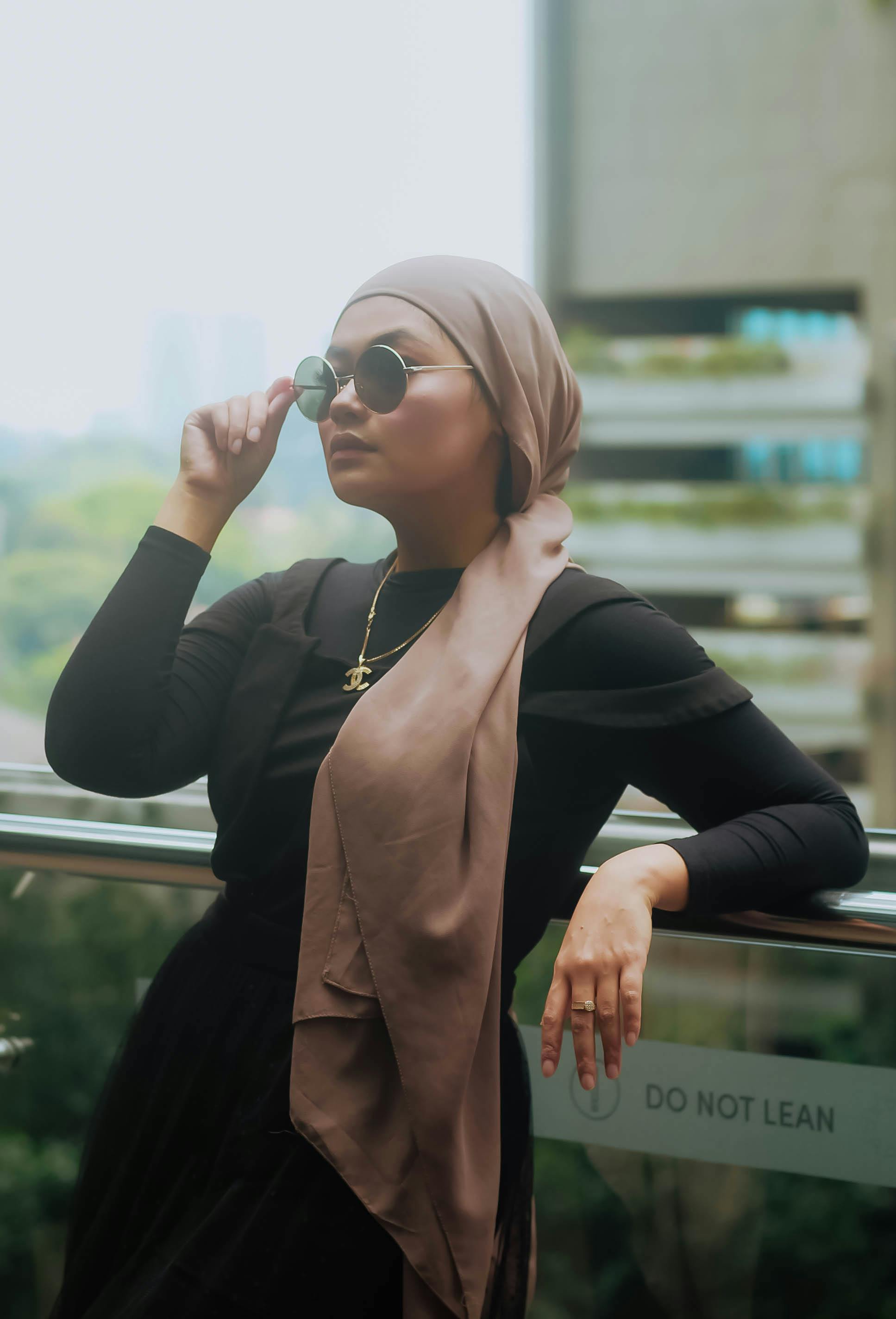 a confident woman exuding elegance in a soft pink hijab and black outfit embodying both strength and grace the subtle details of her attire paired with her poised expression create a p