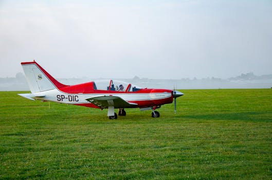 Red and white propeller airplane parked on a green grassy field, ready for flight.