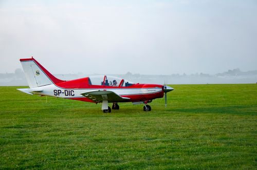 Free Red and white propeller airplane parked on a green grassy field, ready for flight. Stock Photo