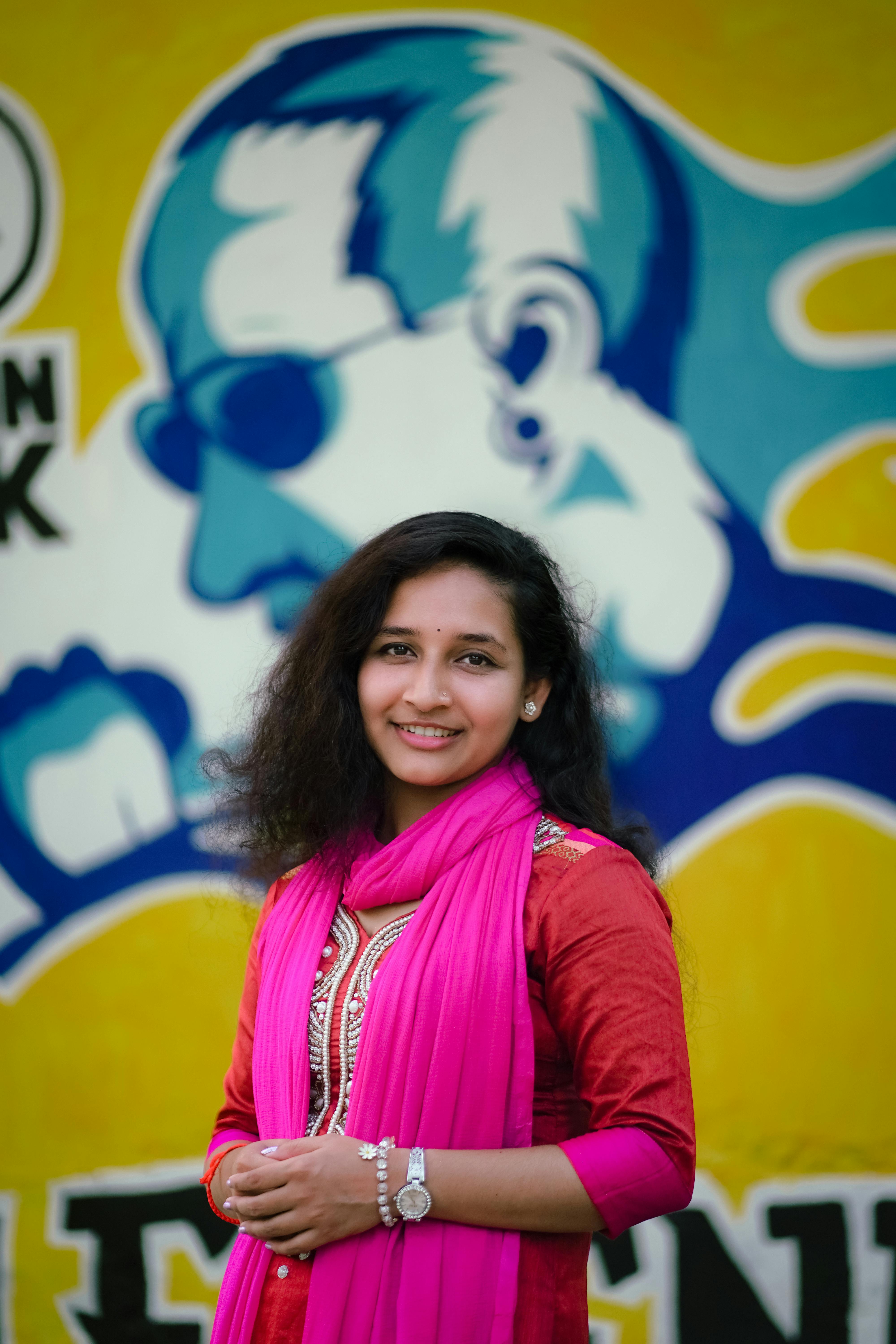 a woman in a pink scarf and pink scarf standing in front of a wall with a mural