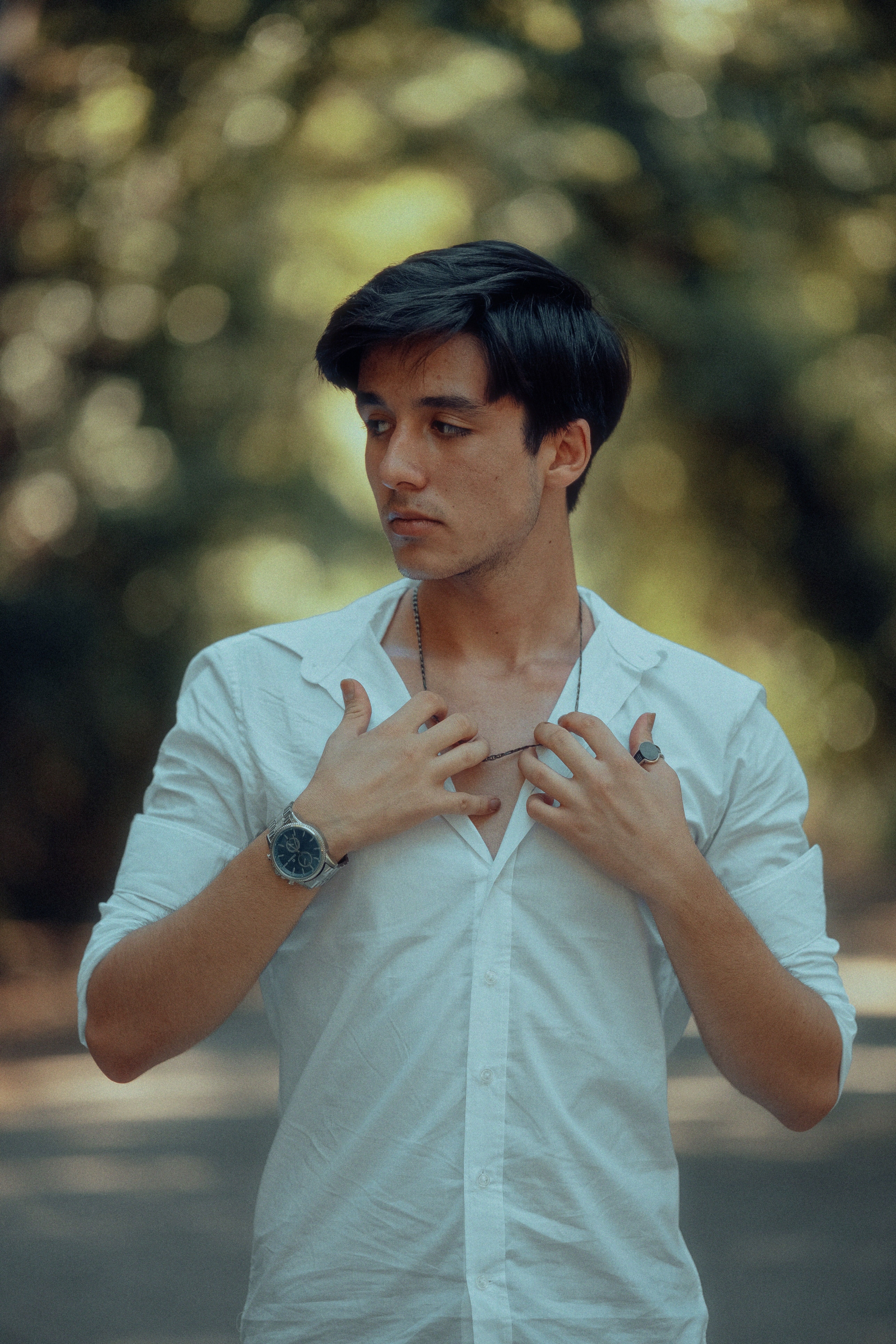 Portrait of a young man in a white shirt standing outdoors with blurred background.