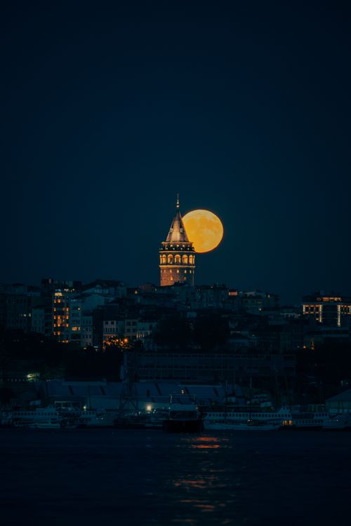 Free Captivating view of Galata Tower with a full moon rising in the night sky. Stock Photo