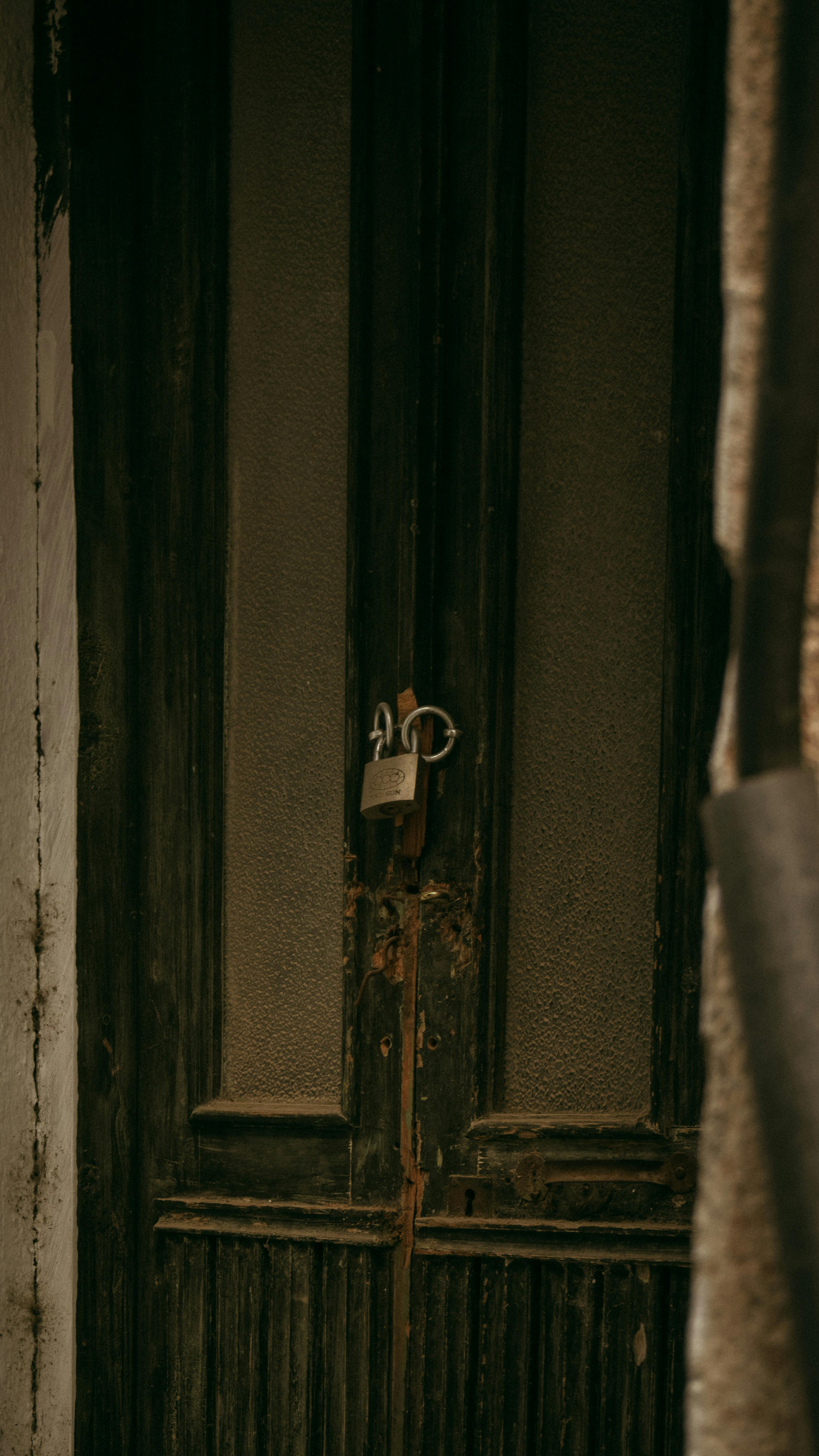 Free Close-up of a locked, aged wooden door in a seemingly abandoned, vintage building. Stock Photo