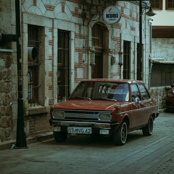 A classic red car parked on an old stone street, exuding a vintage urban vibe.