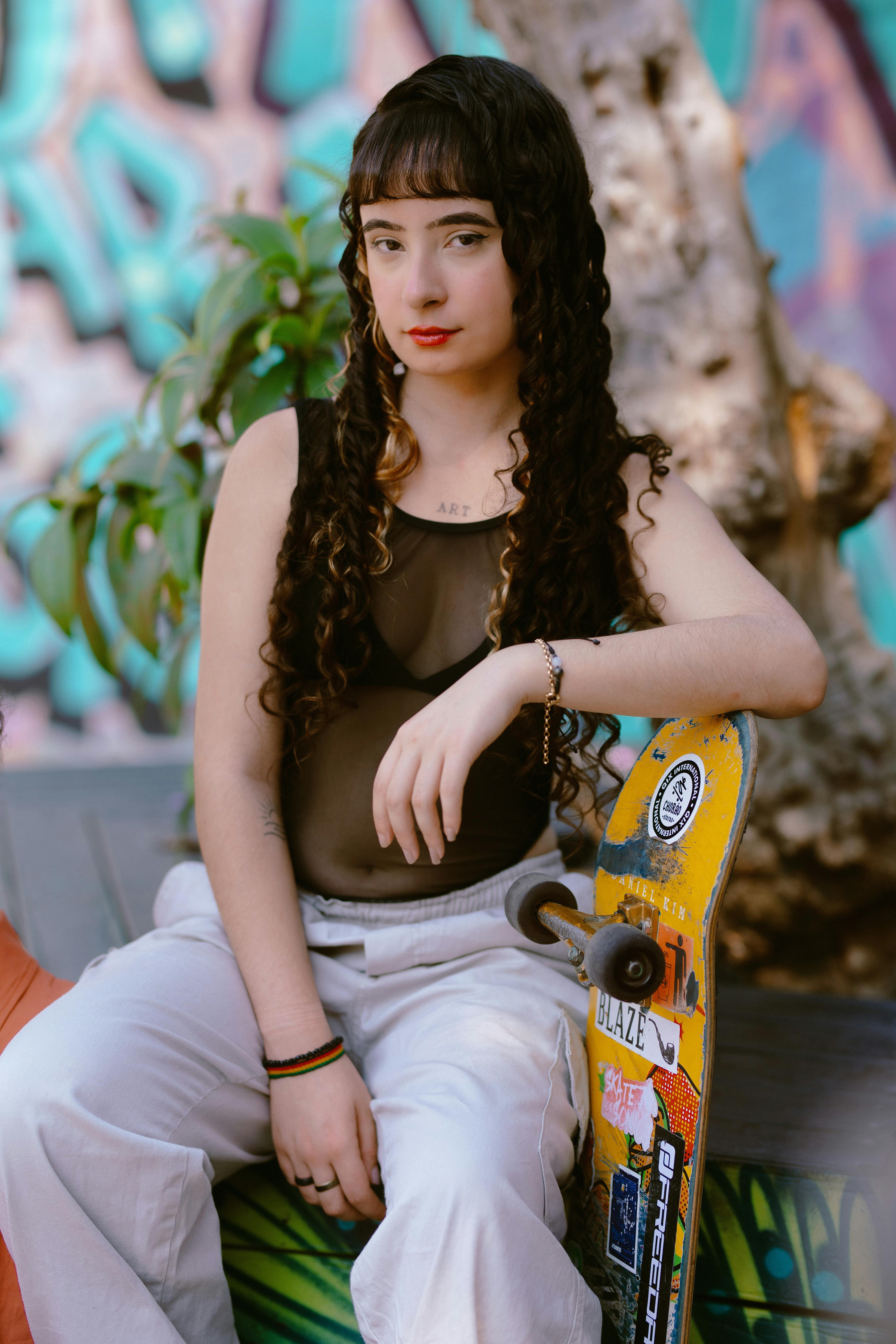 Confident young woman with skateboard sitting by a mural in São Paulo, Brazil.