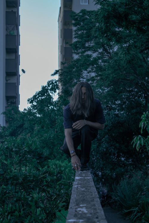 Free A person crouches on a ledge in an urban setting, surrounded by greenery. Stock Photo