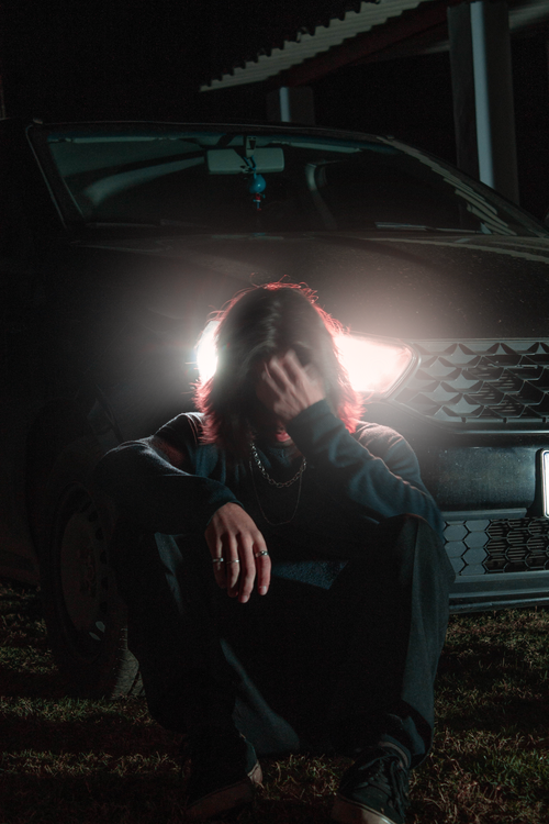 Free A dramatic image of a person sitting against a car with bright headlights at night. Stock Photo
