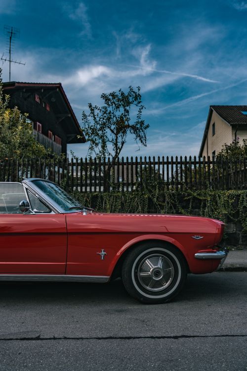 Free Classic red cabriolet parked on urban street with rustic houses in background. Stock Photo
