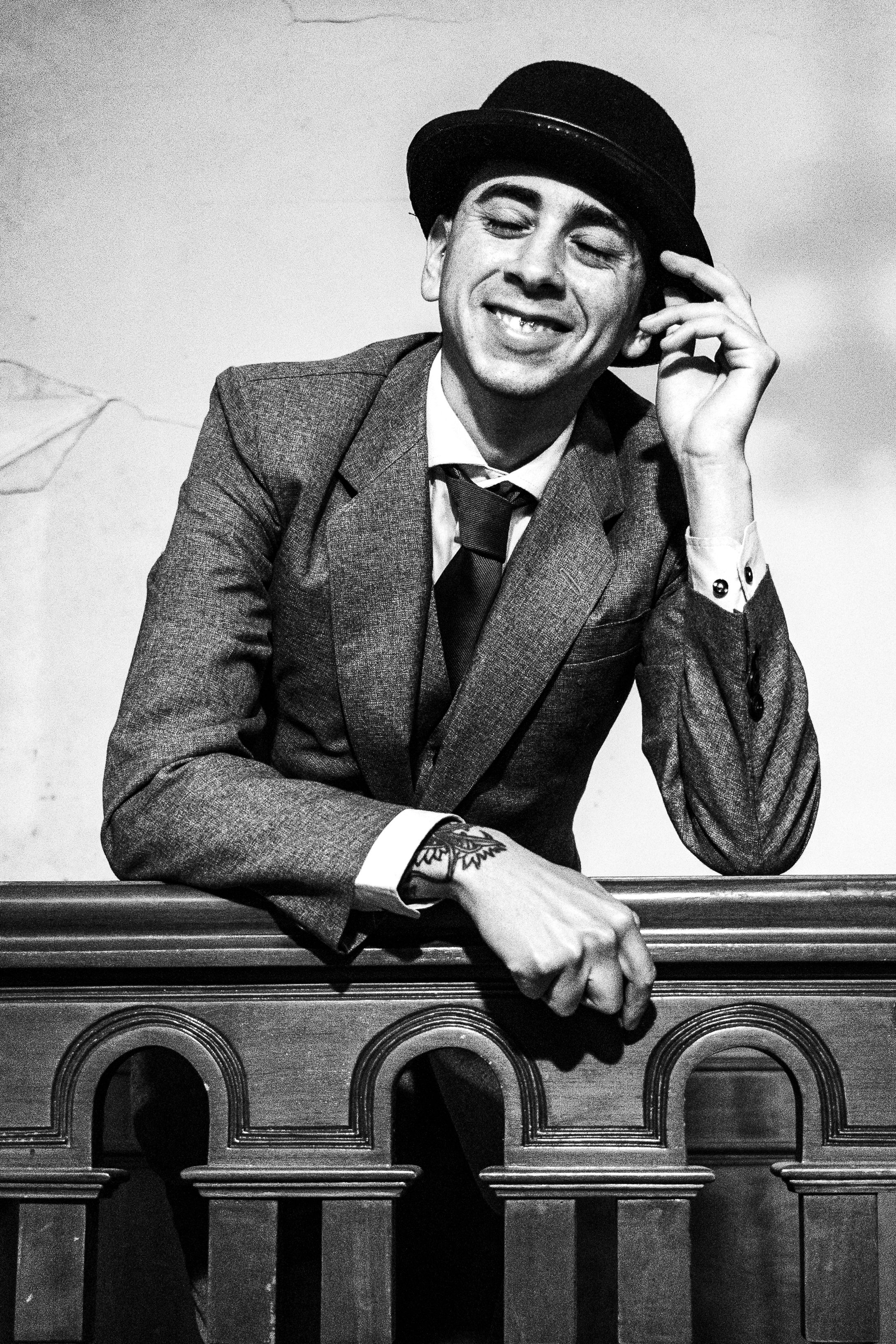 A man in a suit and hat is leaning against a railing · Free Stock Photo