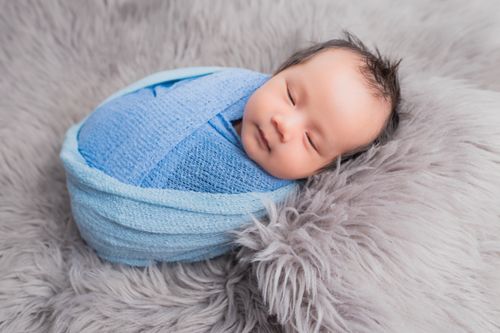 Free Peaceful newborn baby sleeping snugly in a blue wrap on a fluffy surface. Stock Photo