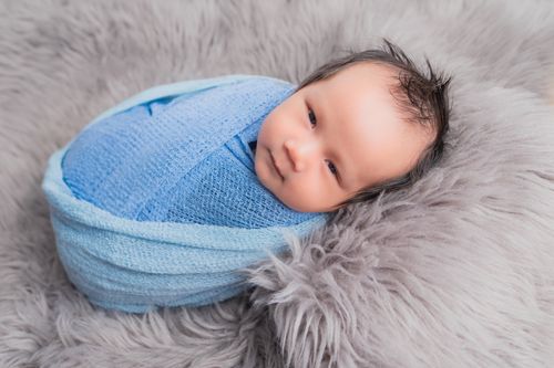 Free Adorable newborn wrapped in a blue blanket lying on a plush fur blanket for a cozy portrait. Stock Photo