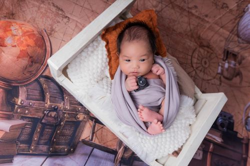 Free Adorable newborn baby wrapped in a blanket on themed background with globe and camera. Stock Photo
