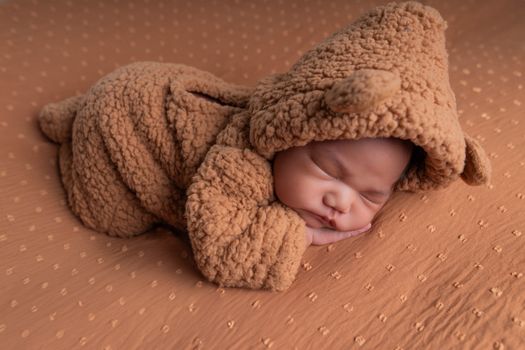 A cute newborn baby peacefully sleeping in a soft, brown bear costume.