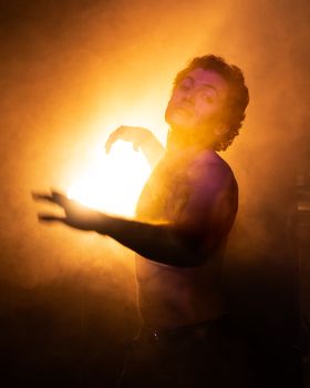 A dynamic silhouette of a shirtless man amidst backlit smoke and warm lighting at an event.