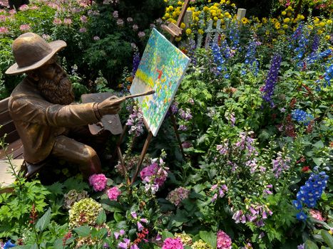 A bronze artist statue paints a canvas amidst a vibrant flower garden.