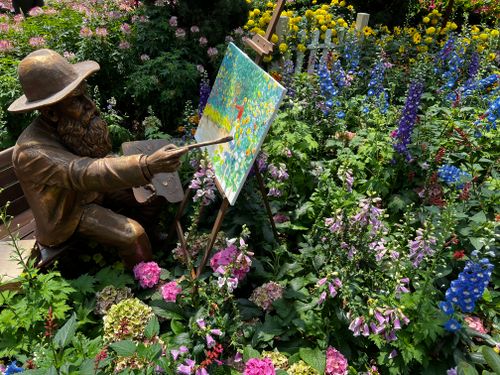 Free A bronze artist statue paints a canvas amidst a vibrant flower garden. Stock Photo