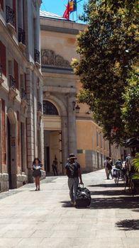 A bustling street in Madrid with pedestrians and sunlight filtering through trees.