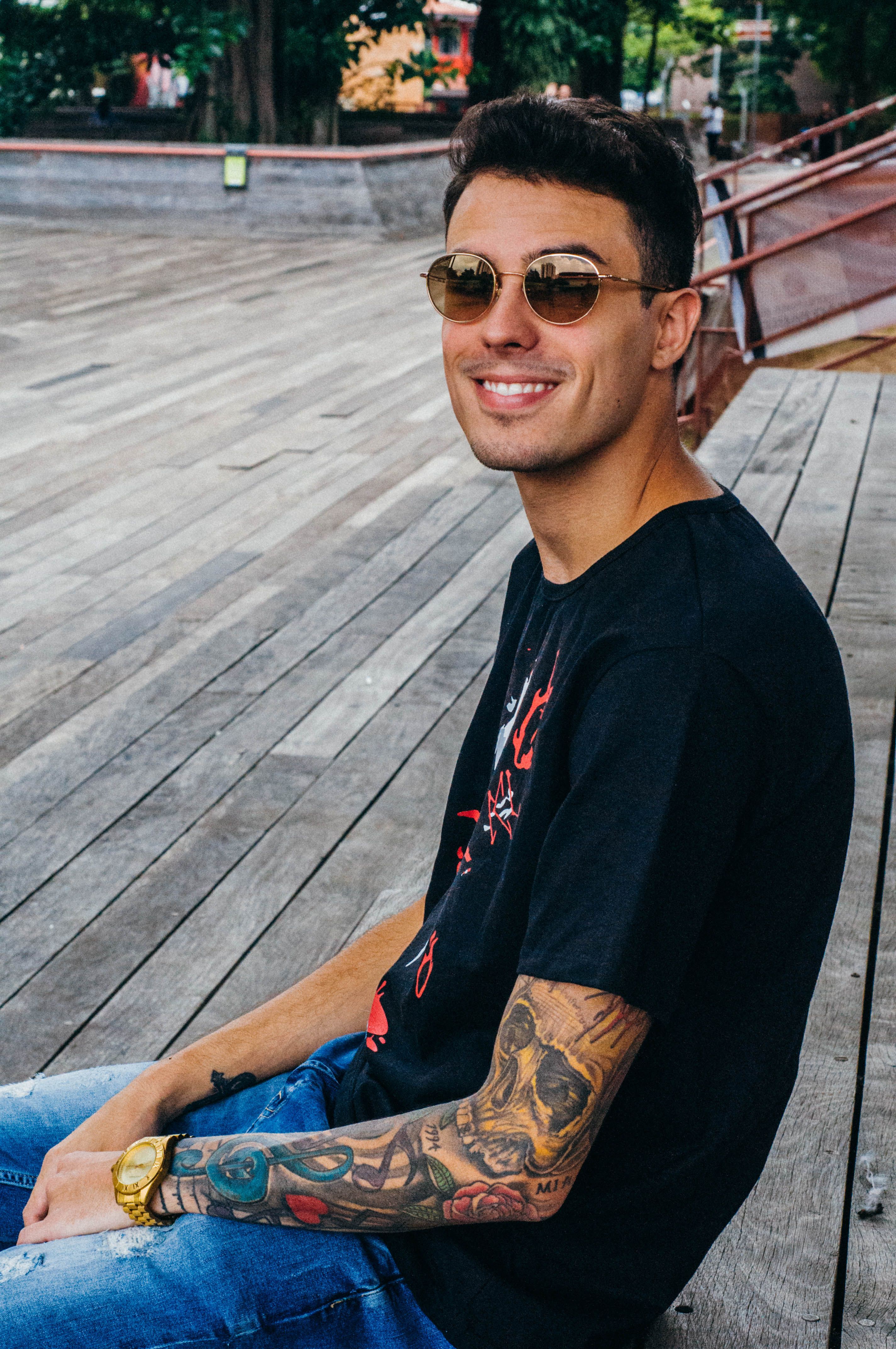 Trendy man with tattoos wearing sunglasses and a tee in a relaxed outdoor setting.