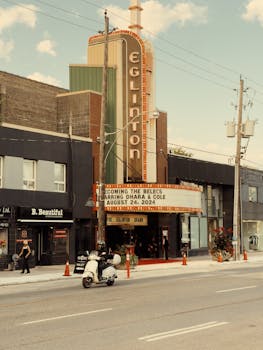 A retro street view of Eglinton Theatre in Toronto with a scooter and pedestrians.