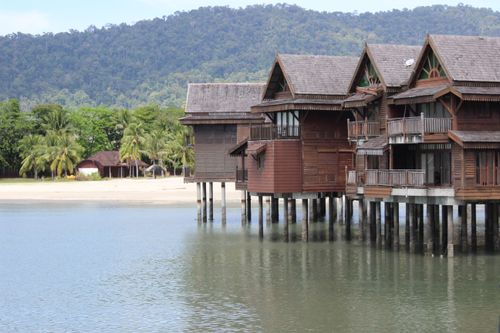 Free Serene wooden beach houses over water with lush tropical background, ideal for travel and architecture themes. Stock Photo