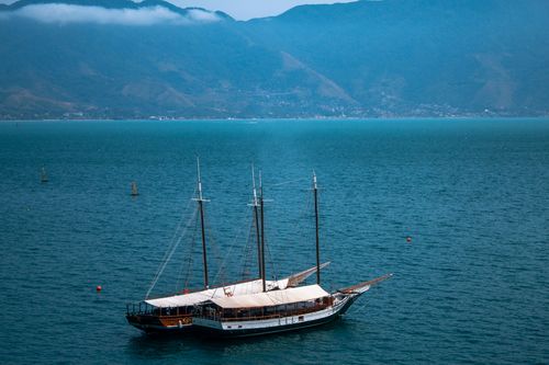 Free A classic sailboat floats peacefully in a tranquil bay with mountains in the background. Stock Photo