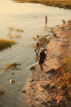 Group of adults walking and relaxing at a peaceful lakeshore during summer sunset.