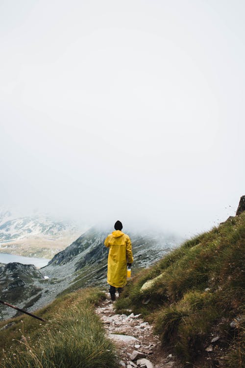 Person Wearing Yellow Raincoat Walking on Grass Pathway