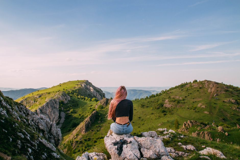 Woman sitting on rock with scenic mountain view in Rimetea, Romania, under clear skies.