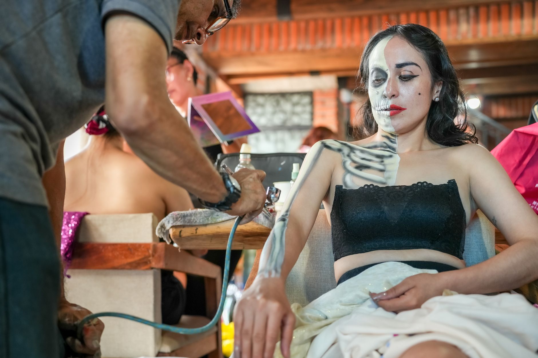 A woman getting traditional Day of the Dead makeup applied indoors in Mexico City.