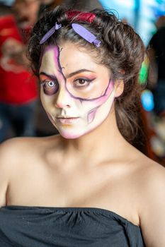 A young woman with artistic Dia de los Muertos makeup posing elegantly indoors in Mexico City.