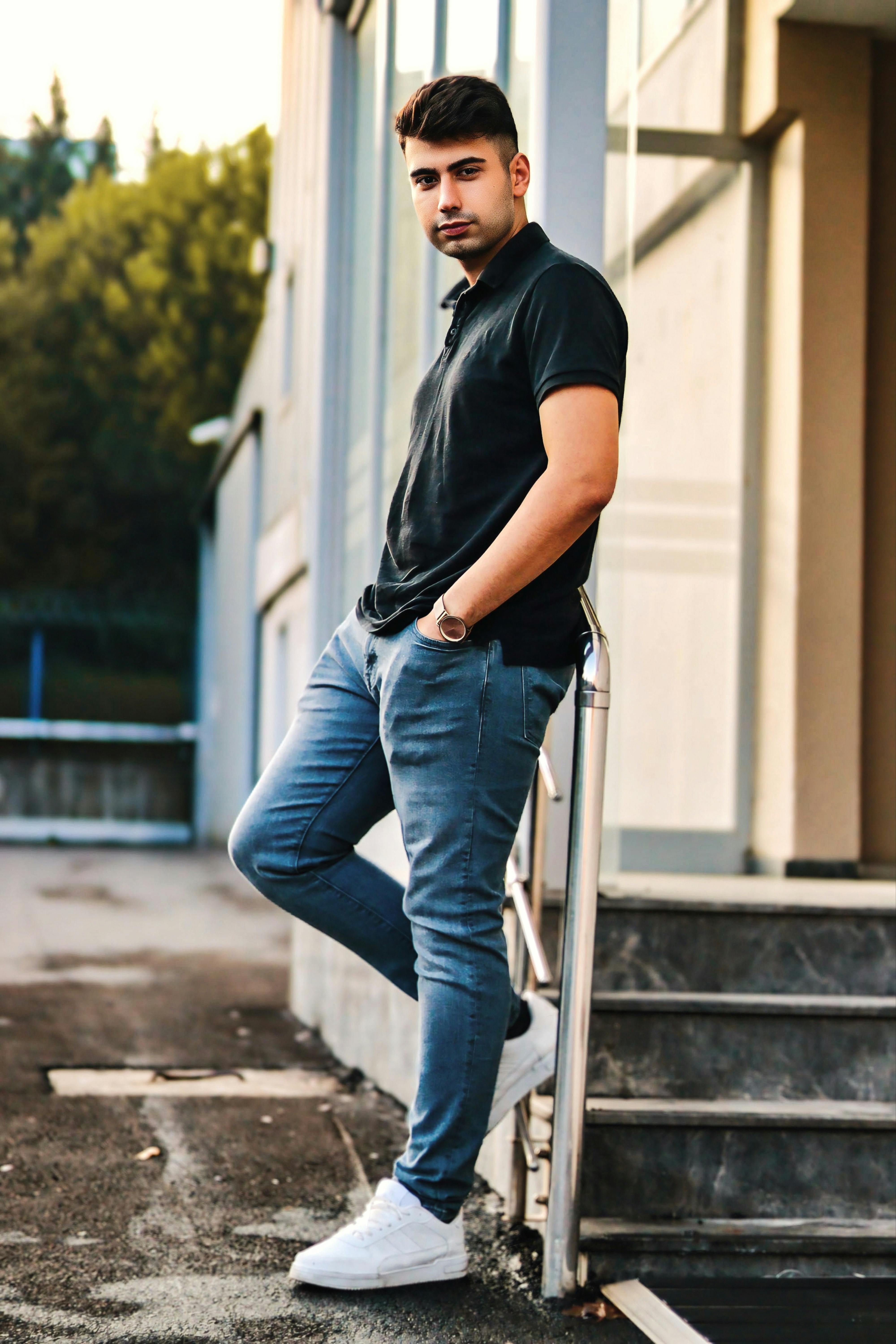 a man in black polo shirt and jeans standing on steps