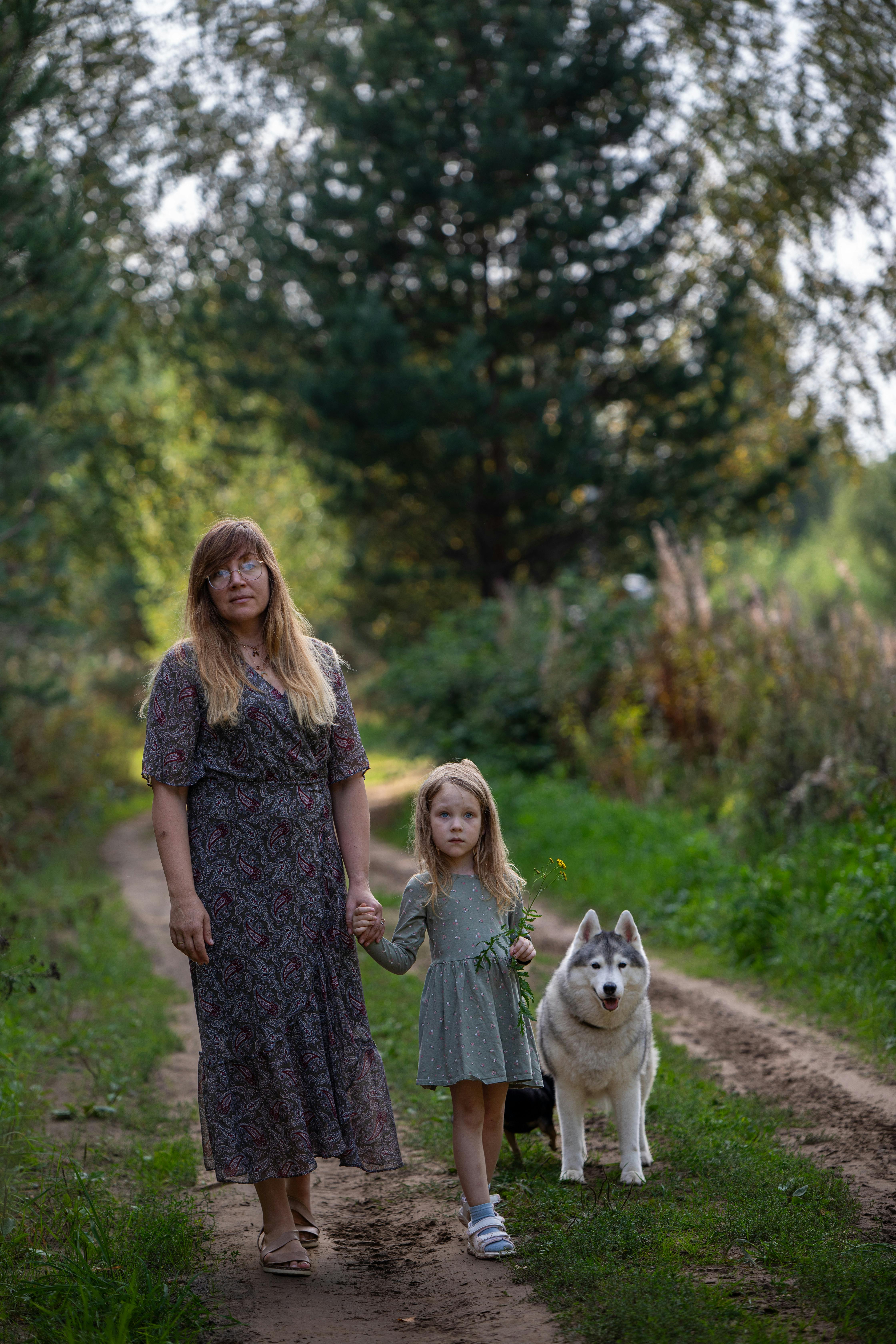 a woman and two children walking down a dirt road with a dog