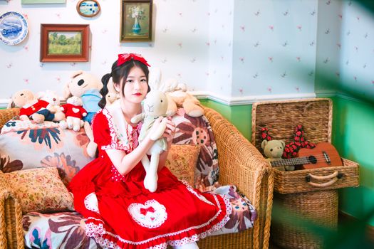 A woman in a red dress sits with a plush toy on a cozy sofa surrounded by stuffed animals.