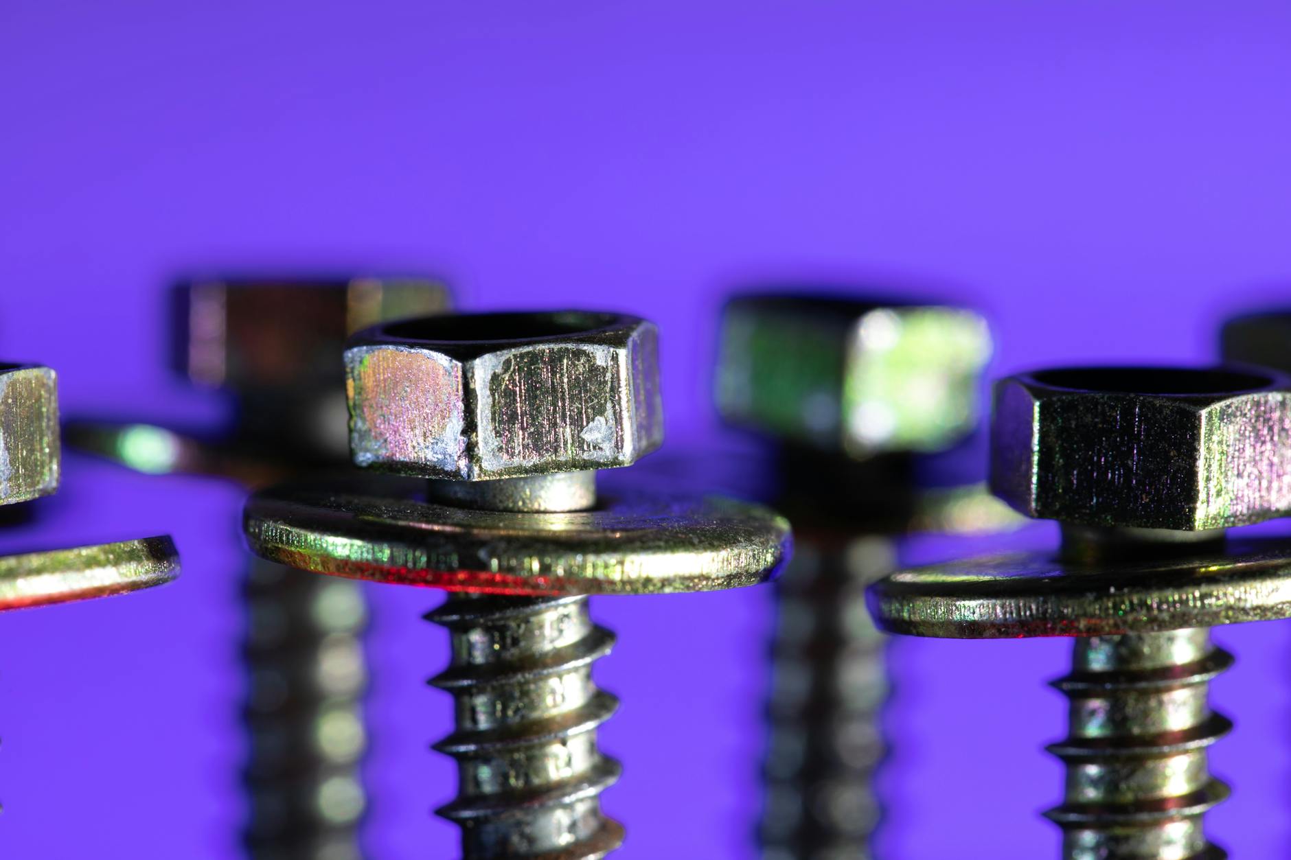 Detailed macro shot of metallic screws and bolts against a striking purple backdrop.