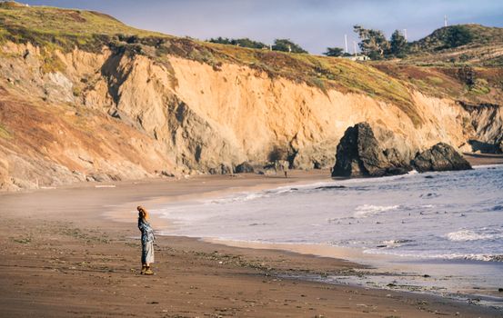 A solitary figure enjoys a quiet moment on a stunning coastal beach with rocky cliffs.