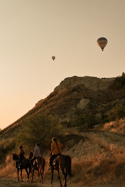 Free Riders on horseback journey through a scenic landscape with hot air balloons overhead at sunset. Stock Photo
