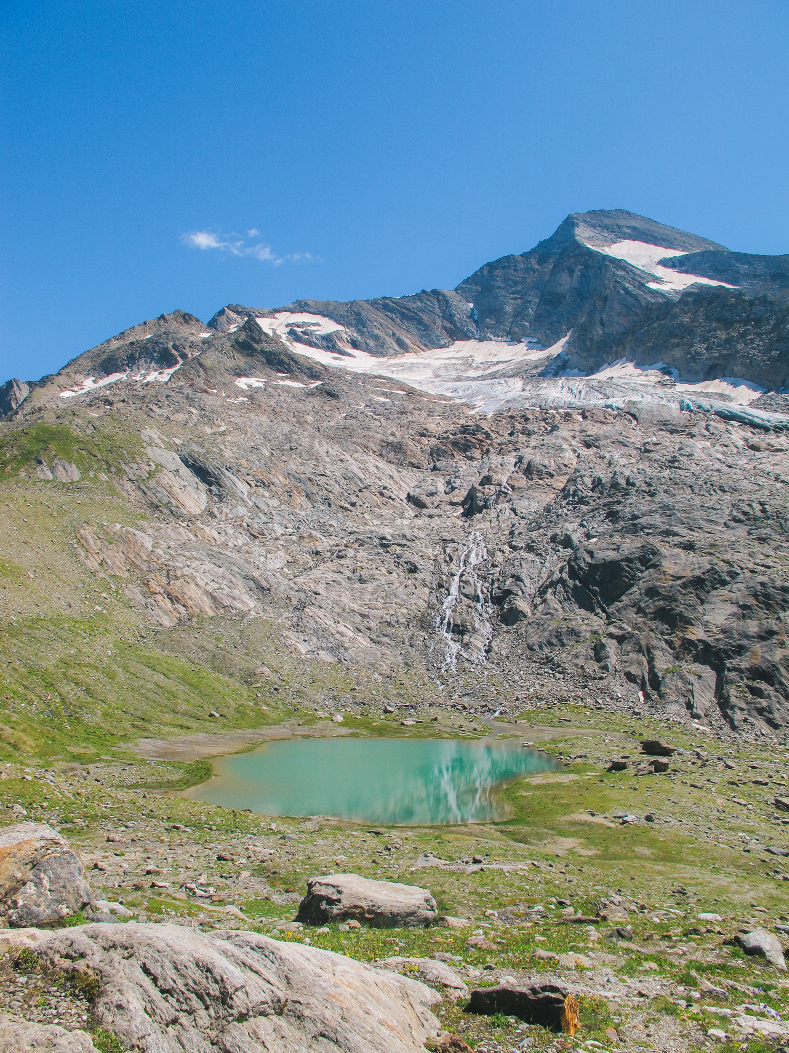 A mountain lake surrounded by rocks and grass · Free Stock Photo