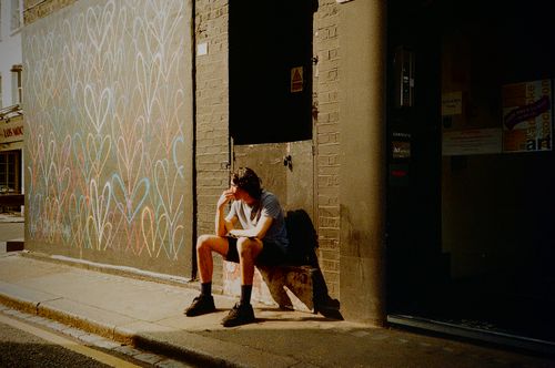 Free A person sits in solitude beside a vibrant graffiti wall on a sunny London street. Stock Photo