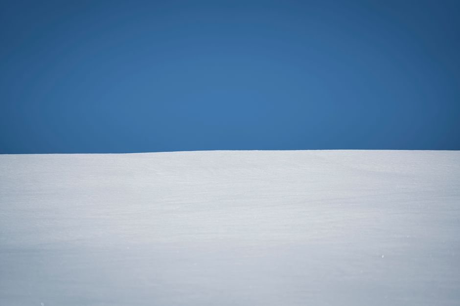 A minimalistic snowfield landscape, capturing the serene beauty of winter under a clear blue sky.
