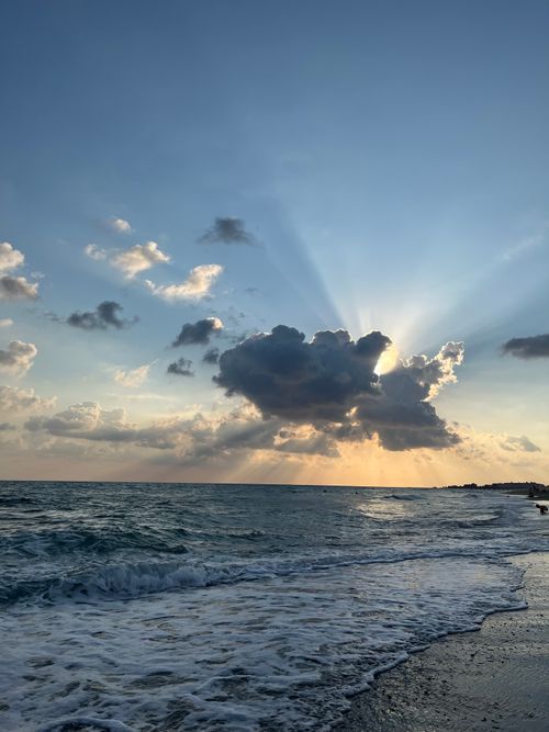 Free A tranquil beach scene with dramatic clouds at sunset over the ocean waves. Stock Photo