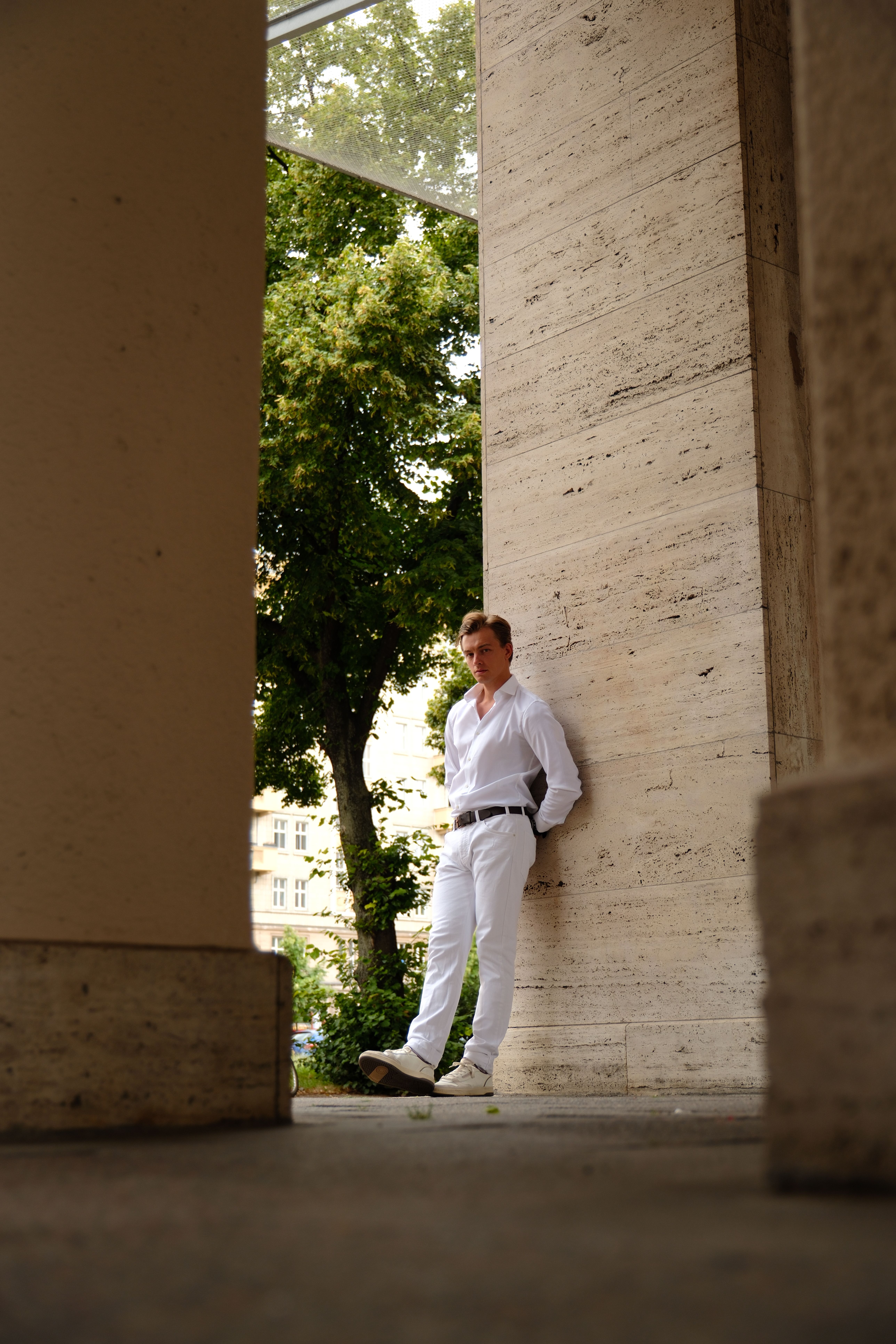 A fashionable man posing against a column in Berlin, captured in natural daylight during summer.