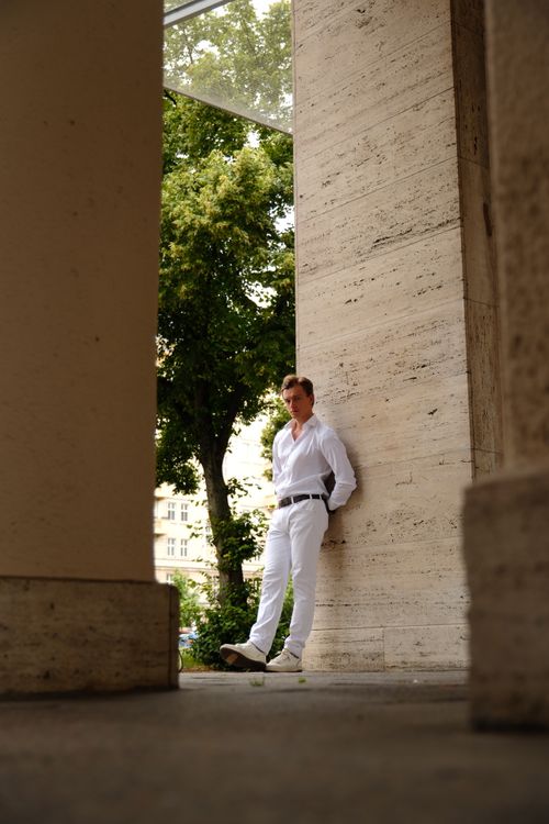Free A fashionable man posing against a column in Berlin, captured in natural daylight during summer. Stock Photo
