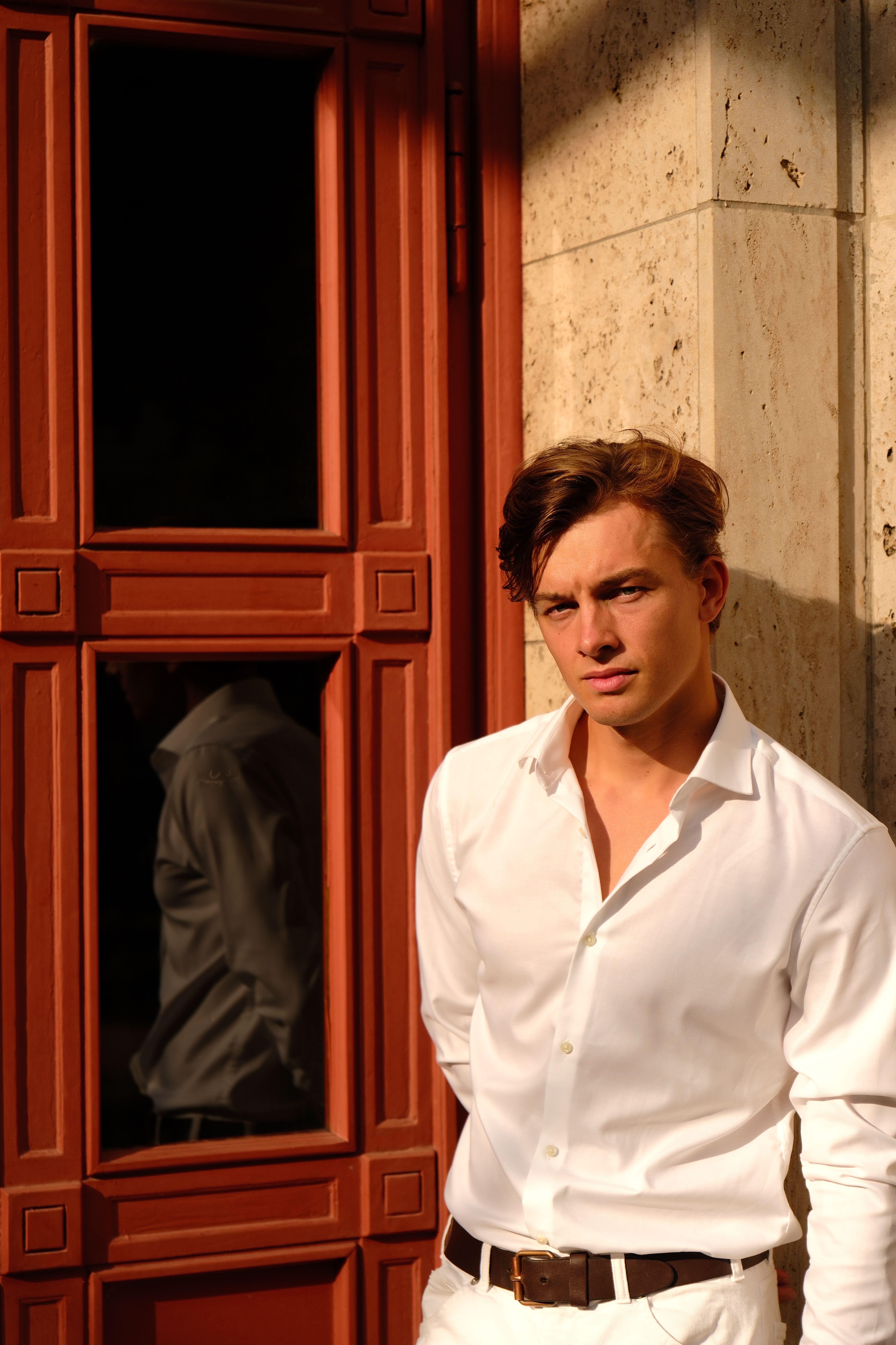 A man in a white shirt and pants leaning against a red door · Free ...
